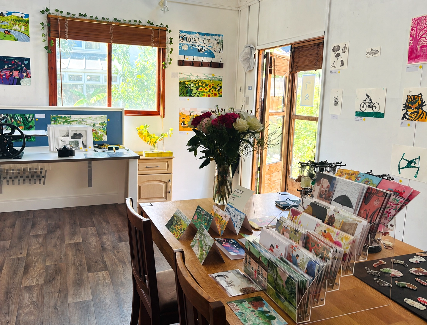 Inside the Swallow Art Cambridge garden studio — cards, prints and flowers on the work table with the garden door open